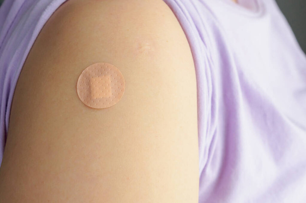 薬注射やワクチン接種後の患者の腕の上に円形の茶色の接着剤包帯を閉じます - 写真・画像