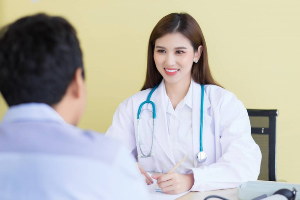 Una bella dottoressa asiatica sorrise e chiese dei sintomi. Rimani in ospedale indossando una veste bianca e uno stetoscopio - Foto, immagini