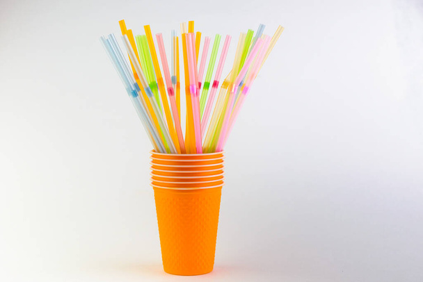 Многоцветные пластиковые трубочки в оранжевой чашке на белом фоне - Фото, изображение