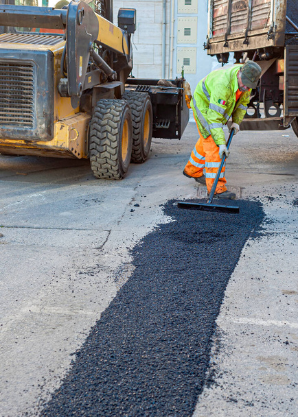 Werknemer reguleren het leggen van nieuw asfalt om een hobbel in de weg. - Foto, afbeelding