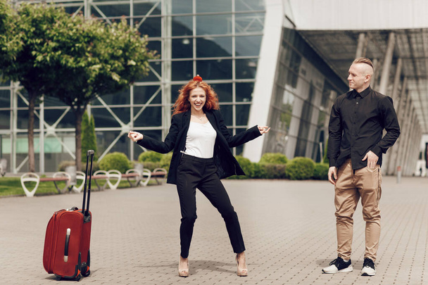 Молодой человек делает предложение, делая предложение очаровательной рыжеволосой девушке в аэропорту. Счастливая женщина танцует с коробкой обручальных колец на голове - Фото, изображение
