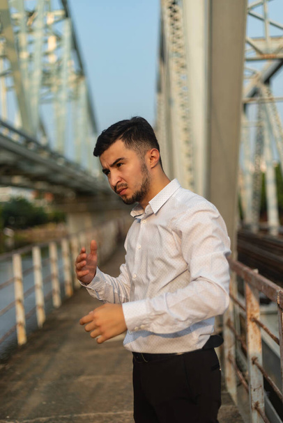 A vertical shot of a young Caucasian man in a white shirt standing on the bridge - Фото, зображення