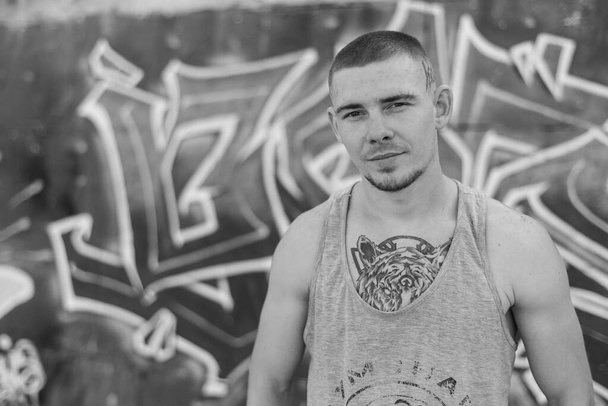 A bully guy in a sports shirt near a wall with graffiti. Black and white photo. BW - Foto, Imagen