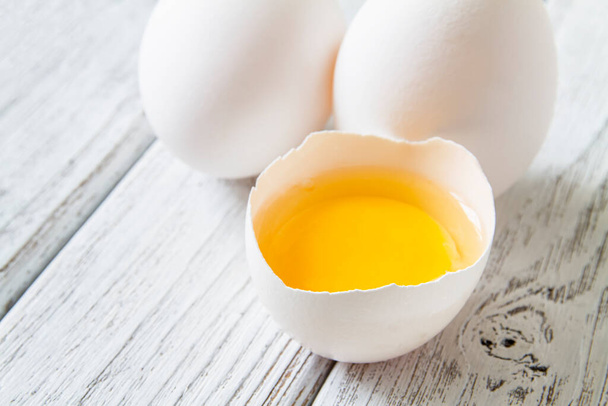 Κοντινό πλάνο με φρέσκα λευκά βιολογικά αυγά κοτόπουλου και κρόκο αυγού σε ανοιχτό ξύλινο φόντο - Φωτογραφία, εικόνα