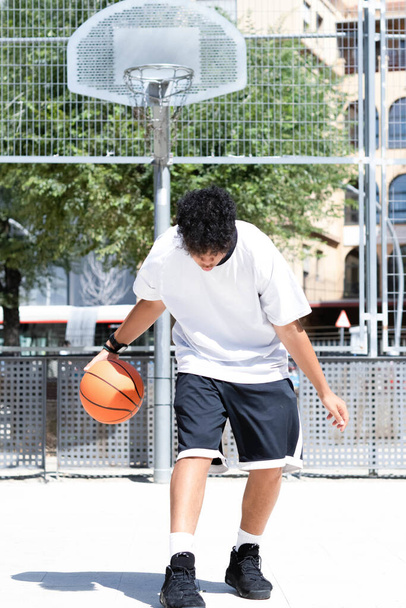 A vertical photo of afro teenage boy throwing the ball to the basket on the basketball court - Zdjęcie, obraz