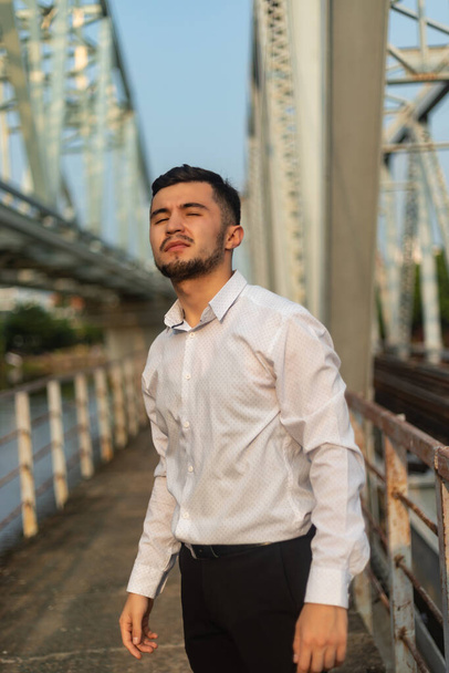 A vertical shot of a young Caucasian man with a white shirt standing on a bridge - Foto, imagen