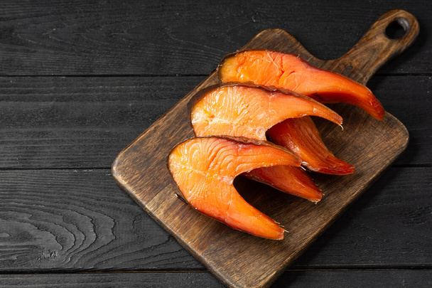 Smoked fish trout. Smoked fish steaks on a serving Board. Sliced smoked trout lay on the wooden kitchen table. Fish close-up. Top view with space for text - Photo, Image