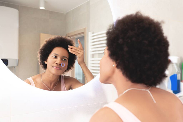 Woman checking her hair in bathroom mirror at home - Fotó, kép
