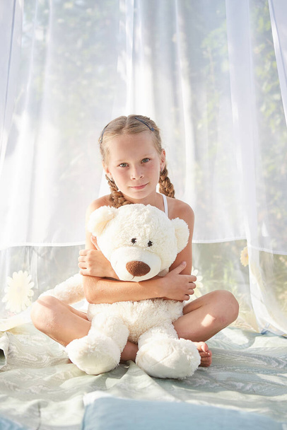 Little girl in white chiffon tent with toy. Childhood, tenderness, beauty - Photo, Image
