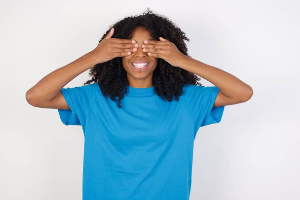 Fiatal afrikai nő göndör haj visel alkalmi kék ing áll ellen fehér háttér borító szemek kezek mosolygós vidám és vicces. Vak fogalom. - Fotó, kép