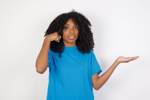 Jovem africana com cabelo encaracolado vestindo camisa azul casual em pé contra fundo branco confuso e irritado com a palma aberta mostrando espaço de cópia e apontando o dedo para a testa. Pense nisso.
. - Foto, Imagem