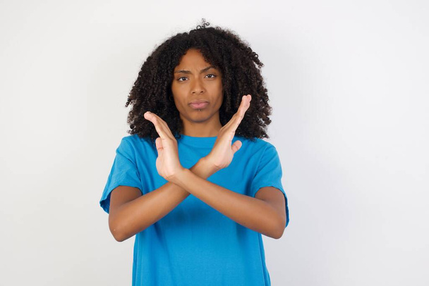 Jovem mulher africana com cabelo encaracolado vestindo camisa azul casual em pé contra fundo branco Expressão de rejeição cruzando braços fazendo sinal negativo, rosto zangado
 - Foto, Imagem