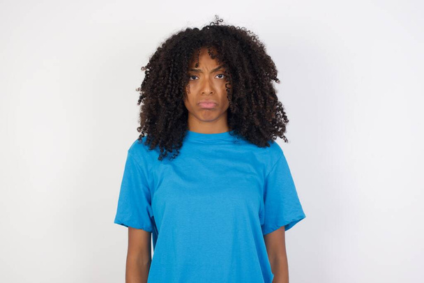 Retrato de disgustado disgustado Mujer africana joven con el pelo rizado con camisa azul casual de pie sobre fondo blanco frunce el ceño cara como va a llorar, siendo descontento e infeliz como no puede lograr objetivos, Hombre joven decepcionado tiene problemas - Foto, Imagen