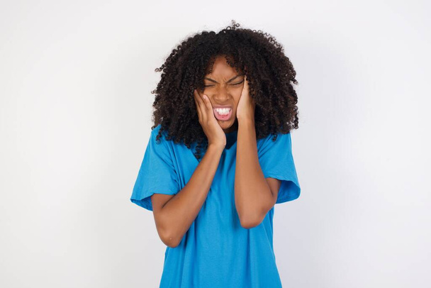Verzweifelt weinende junge Afrikanerin mit lockigem Haar, lässig blauem Hemd vor weißem Hintergrund, die nach einem Streit mit Frau oder Freundin in Depressionen steckt, sieht gestresst aus, runzelt die Stirn. Weibchen fühlt sich einsam und ängstlich - Foto, Bild