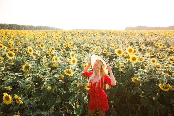 beautiful young female in a red dress with a hat in a field with sunflowers - Foto, afbeelding