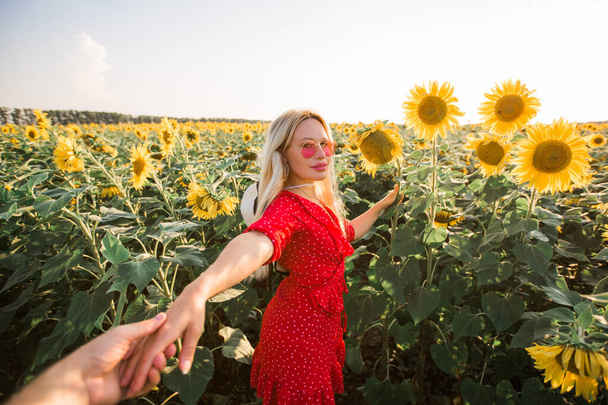 beautiful young female in a red dress in sunglasses in a field with sunflowers - Foto, immagini