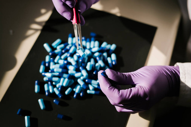 Mani di uno scienziato che lavora con alcune capsule blu - Foto, immagini