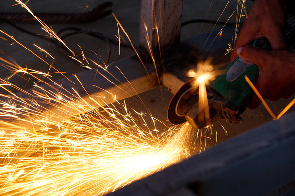 Onveilige arbeider snijden van metalen constructie zonder bescherming Uniform met elektrische wiel slijpmachine in de bouwplaats. - Foto, afbeelding