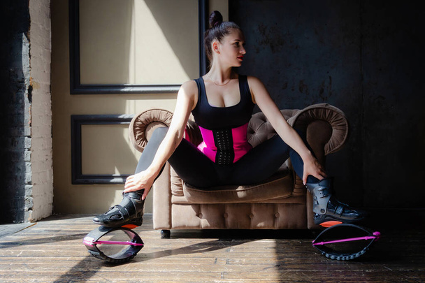 Beautiful fit caucasian woman posing in shoes for kangoo jumping sitting on armchair - Fotoğraf, Görsel