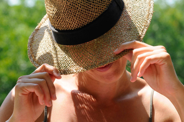 femme portant un chapeau de paille pour la protection solaire, fond vert flou - Photo, image