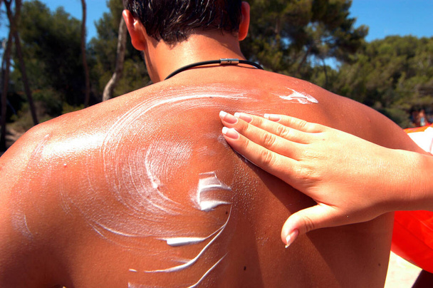 back of a man gets rubbed with suncream, skin protection on hot summer day - Photo, Image