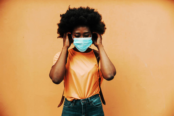 Młoda atrakcyjna afrykańska kobieta z kręconymi włosami zakładająca maskę na twarz, aby zapobiec rozprzestrzenianiu się wirusa korony / covid 19. - Zdjęcie, obraz