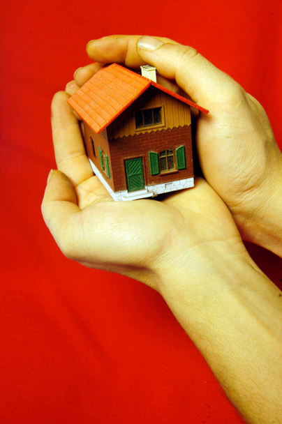 manos sosteniendo un edificio unifamiliar unifamiliar en miniatura, fondo rojo - Foto, imagen