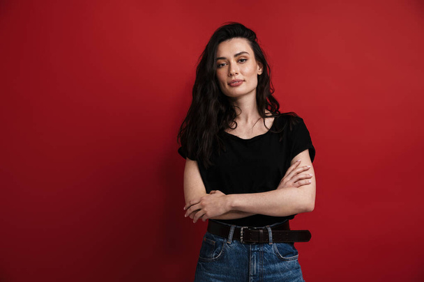 Photo of brunette nice woman in casual t-shirt posing and looking at camera isolated over red background - Foto, immagini