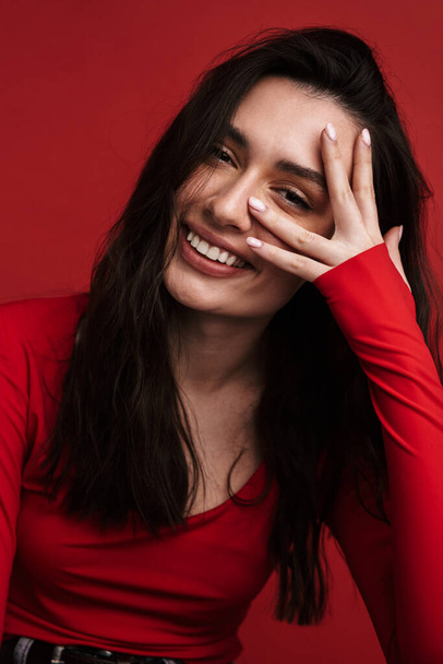 Photo of brunette funny woman smiling and looking at camera isolated over red background - Foto, immagini