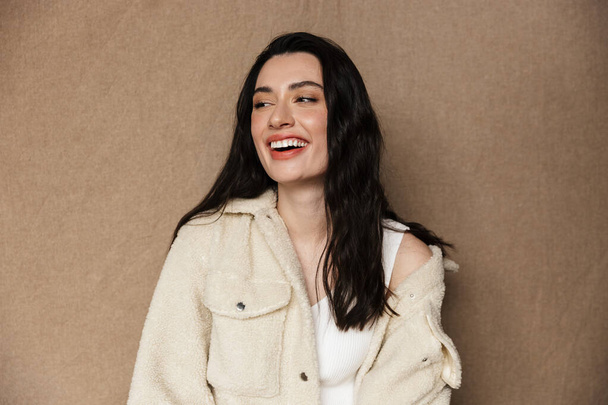 Photo of joyful young woman in jacket laughing and looking aside isolated over beige background - Foto, Imagem