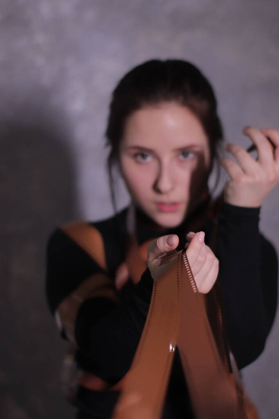 portré egy barna lány egy fekete garbó csomagolva egy film szalag - filmtekercs egy szürke fal háttér - Fotó, kép
