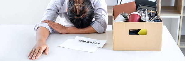 Images of business woman carrying packing up all his personal belongings and files into a brown cardboard box has frustrated and stressed to resignation and signing cancellation contract letter. - Foto, Imagen