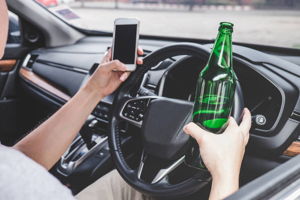 Young asian man drives a car with drunk a bottle of beer and using smartphone behind the wheel of a car. - Photo, Image