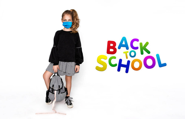 Вірус коронавірусу ковідо-19. Повернутися до концепції школи. Симпатична дівчинка з рюкзаком та хірургічною маскою під час коронавірусу ходить до школи ізольовано на білому - Зображення
 - Фото, зображення