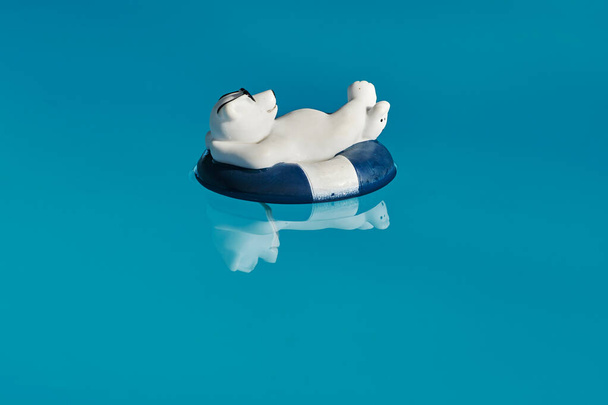 Zwembaddecoratie in de vorm van een relaxte ijsbeer met zonnebril en een zwemring op blauw water. - Foto, afbeelding