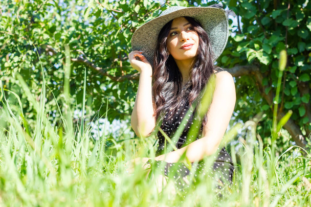 young woman in a straw hat sitting on the grass in the garden - Foto, immagini