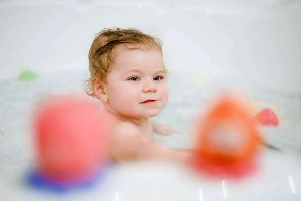 Linda menina adorável tomando banho espumoso na banheira. Criança brincando com brinquedos de borracha de banho. Criança bonita se divertindo com brinquedos coloridos de goma e bolhas de espuma - Foto, Imagem