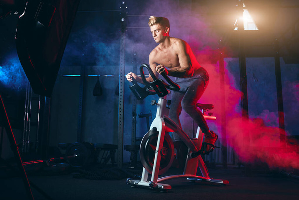 Cardio Workout. Shirtless man training on bicycle, cycling mashine in gym - Фото, изображение
