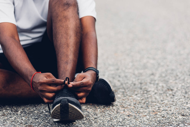 Close up Asian sport runner black man sitting shoelace trying running shoes getting ready for jogging and run at the outdoor street, health exercise workout concept - Photo, image