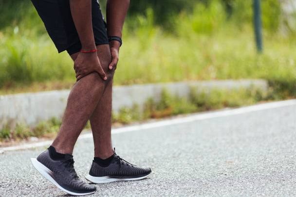 Asian young athlete sport runner black man stand wear feet shoe active running training at outdoor he use hands hold on his knee pain while running, healthy exercise injury osteoarthritis from workout - 写真・画像