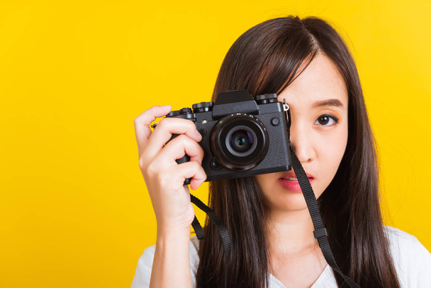 Portrait of happy Asian beautiful young woman photographer taking a picture and looking viewfinder on retro digital mirrorless photo camera ready to shoot, studio shot isolated on yellow background - Foto, Bild