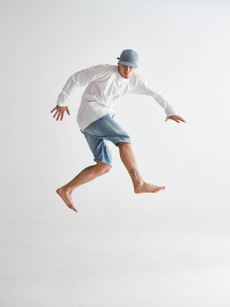 Cool young guy breakdancer jumps dancing hip-hop isolated on white background. Dance school poster. Break dance lessons - Fotografie, Obrázek