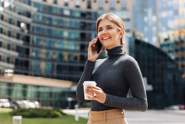 Young attractive woman talking on a mobile phone against the background of a business center - Foto, imagen