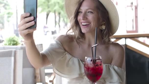 Vrouw in een hoed met videogesprek, terwijl ze rust in een café. - Video