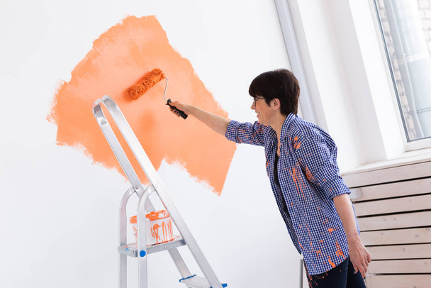 Mulher de meia-idade muito sorridente pintando parede interior de casa com rolo de pintura. Redecoração, renovação, reparação de apartamentos e conceito de refresco
. - Foto, Imagem