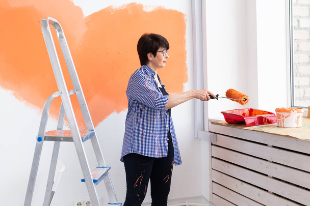 Hermosa mujer de mediana edad pintando la pared con rodillo de pintura. Retrato de una joven mujer hermosa pintando la pared en su nuevo apartamento. Concepto de reacondicionamiento y renovación. - Foto, Imagen