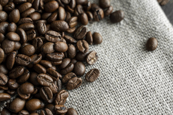 Coffee beans on a linen textile and on a wooden table background. Fresh arabica coffee beans. - Fotografie, Obrázek
