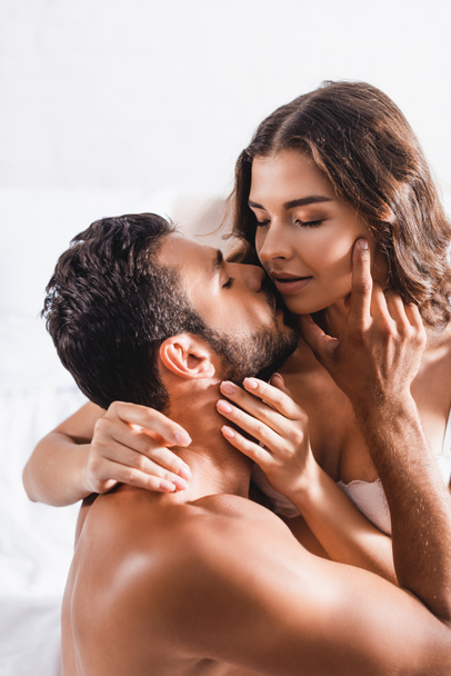 Muscular man kissing and touching face of woman in lace bra on bed  - Zdjęcie, obraz