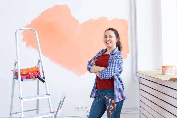 Hermosa mujer pintando la pared con rodillo de pintura. Retrato de una joven mujer hermosa pintando la pared en su nuevo apartamento. Concepto de reacondicionamiento y renovación. - Foto, imagen
