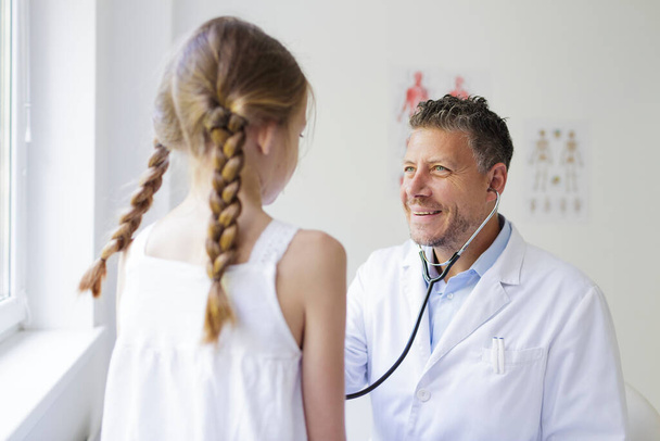 male doctor with three-day beard examines young girl with a stethoscope - Fotoğraf, Görsel